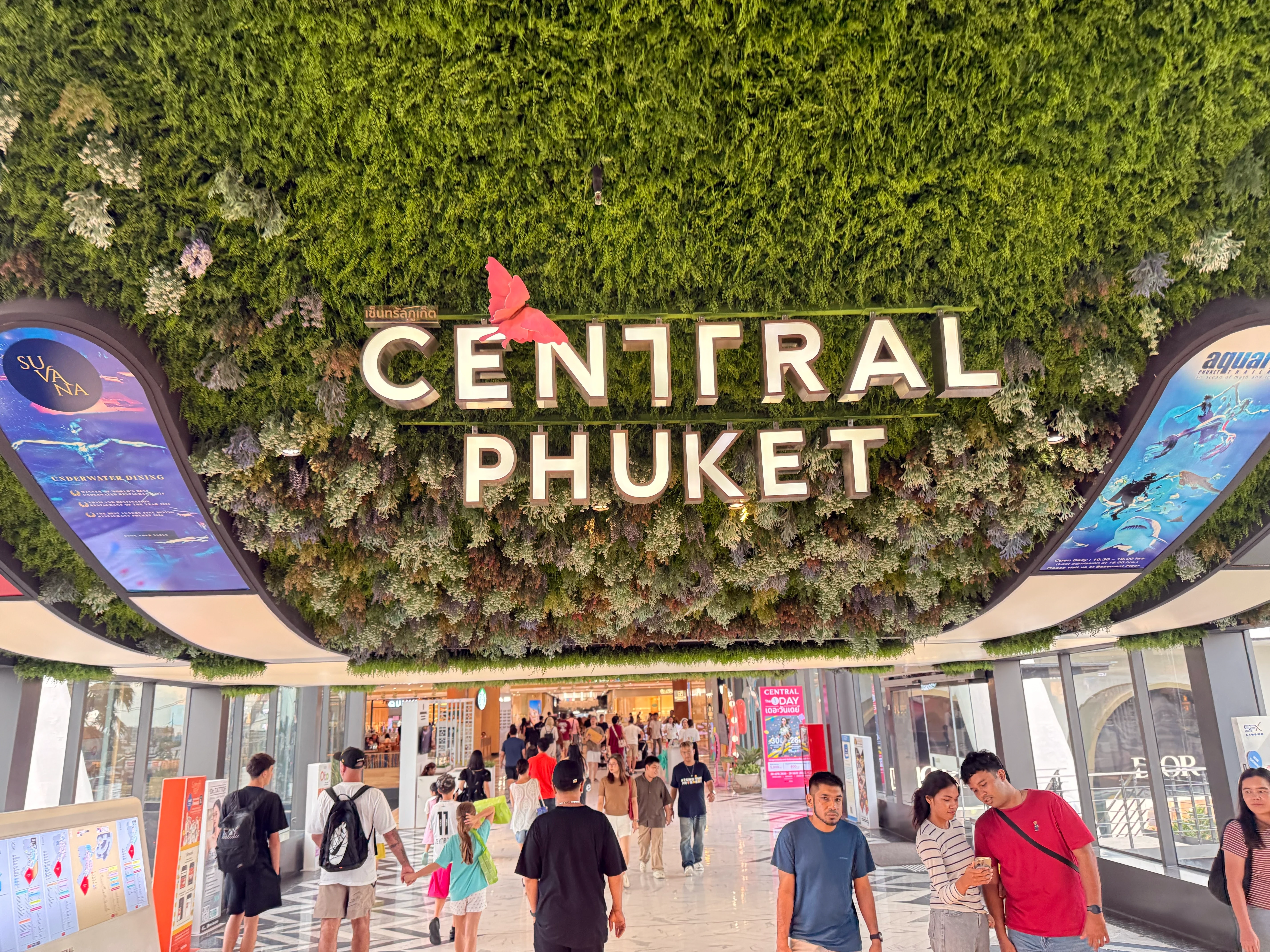 A mall entrance under a deep green living wall, with people walking through in the afternoon