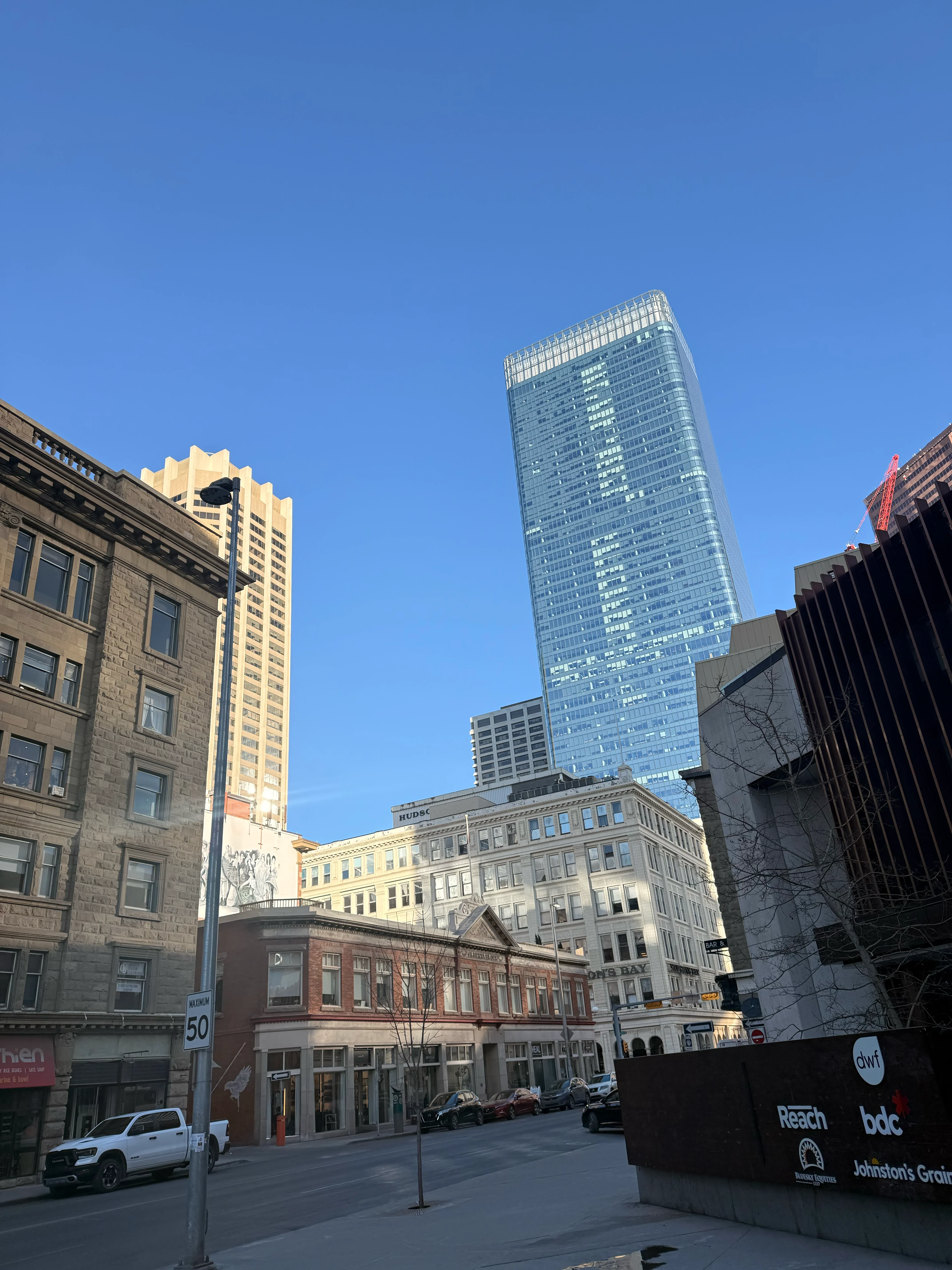 A glass tower above older brick and sandstone buildings, shot looking up from the street