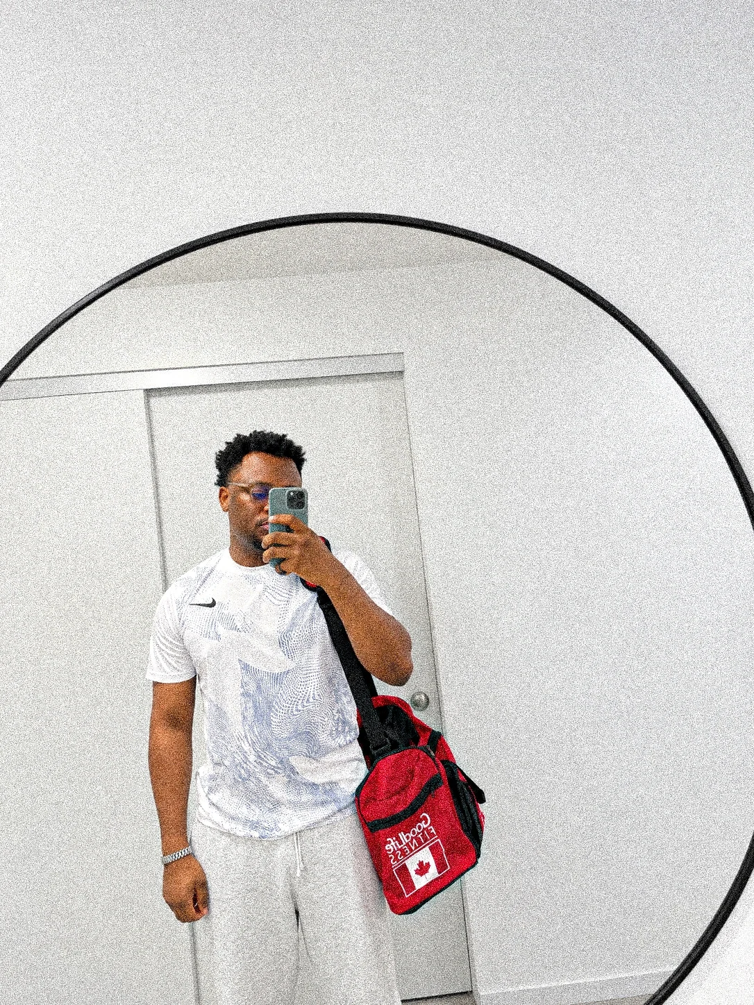 Oluwayemi in a round mirror in white sportswear, with a red duffel bag over his shoulder