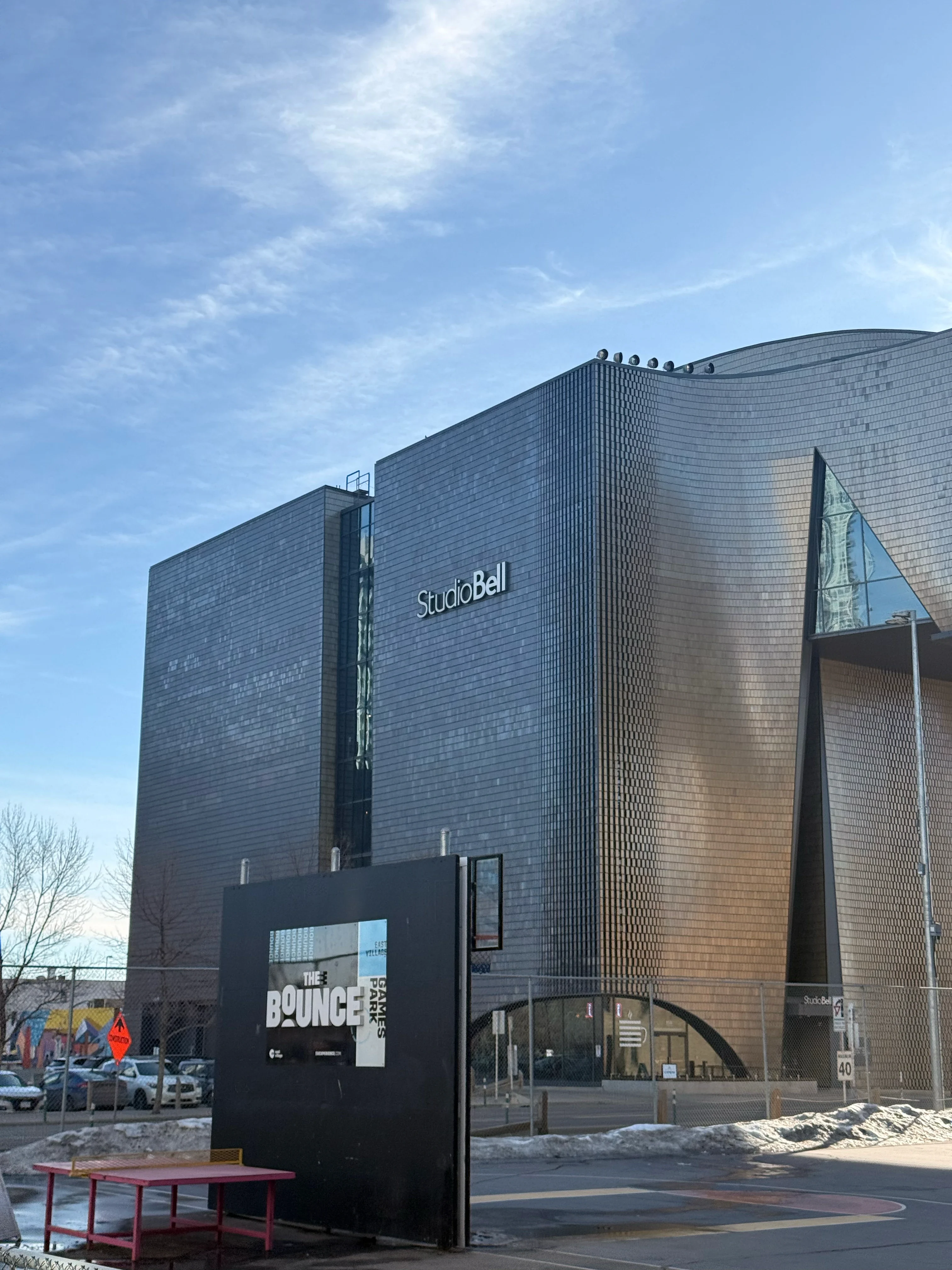 A curved building clad in dark and bronze tile, rising against a clear winter sky